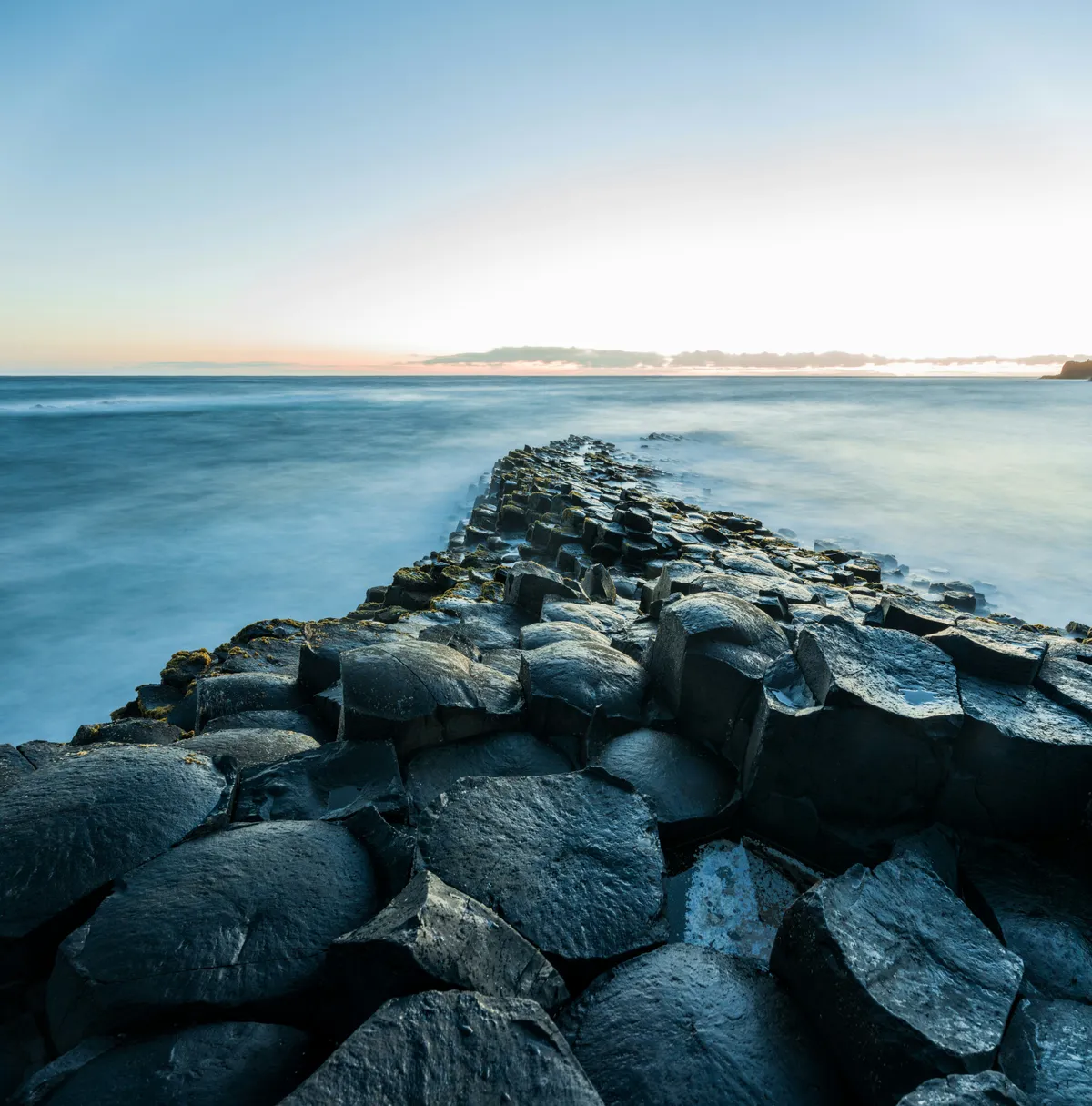 The hexagonal basalt columns of the Giant's Causeway stretching into the distance, Co. Antrim — ancient foundations that predate everything built on top of them.